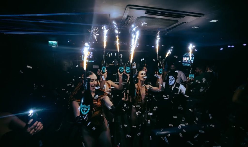 Bottle girls holding champagne bottles and sparklers for a champagne show inside Funky Buddha club in London.